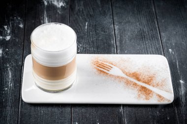 Kahve fincanı macchiato ya da kapuçino. Masada koyu bir arka planda köpük var.