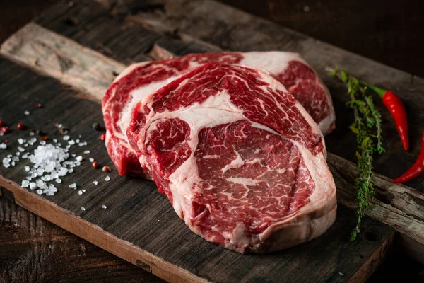 Fresh raw beef rib eye steak with red pepper and herbs on a wooden background