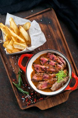 Dilimlenmiş sığır filetosu az pişmiş, tabakta sos ve ahşap zeminde patates kızartması.