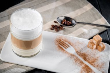 Kahve fincanı macchiato ya da kapuçino. Masada koyu bir arka planda köpük var.