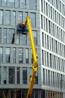 Cam temizleyicisi, sarı bir vinçle bir ofis binasının cam cephesinde çalışır.
