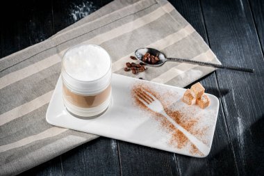 Kahve fincanı macchiato ya da kapuçino. Masada koyu bir arka planda köpük var.