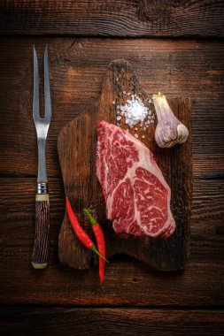 Çiğ biftek Chuck rulo sığır eti ahşap bir tahta üzerinde baharatlar ve bir et çatalı, üst görünüm