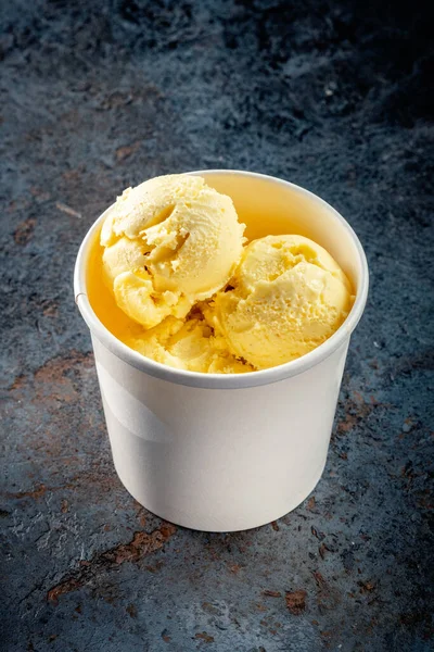 Yellow Lemon ice cream balls in a white paper Cup on a gray stone background