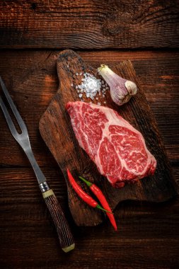 Tahta üzerinde çiğ demir biftek, baharatlar ve et çatalı.