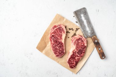 Kağıt üzerinde iki çiğ mermer biftek ve bir et satırı, üst görünüm ve kopyalama alanı.