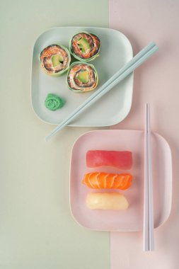 Suşi nigiri ve salatalık ve somonla birlikte yeşil arka planda yemek çubukları olan bir tabak.