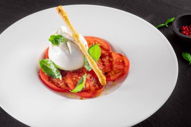 Burrata peyniri ve domates salatası, koyu arkaplanda fesleğen ve zeytinyağı.