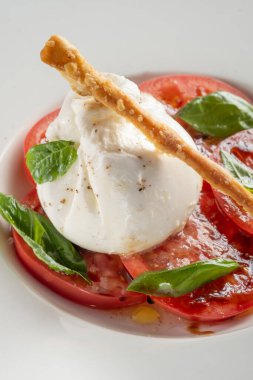 Burrata peyniri ve domates, fesleğen, beyaz tabakta servis edilen yağ, kapat.