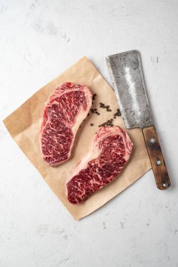 Kağıt üzerinde iki çiğ mermer biftek ve bir et satırı, üst görünüm ve kopyalama alanı.