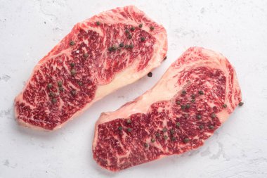 Beyaz taş bir masada tuzlu ve biberli çiğ Wagyu bifteği.