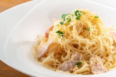 Pastırmalı, peynirli ve otlu spagetti, ahşap arka planda beyaz bir tabakta, yakın plan.