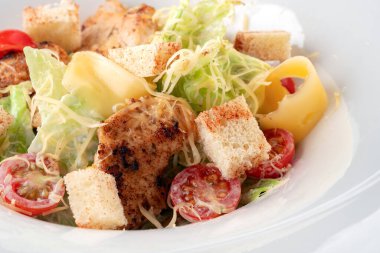 Klasik Sezar Salatası, ızgara tavuk, kızarmış ekmek, kiraz domatesleri ahşap bir masada beyaz tabakta, yakın çekim.