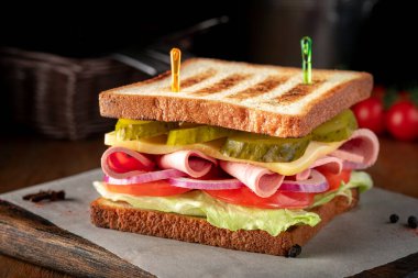 Peynirli, jambonlu, salatalıklı, domatesli ve ekmek ekmekli büyük bir sandviç.