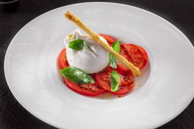 Burrata peyniri ve domates salatası, koyu arkaplanda fesleğen ve zeytinyağı.