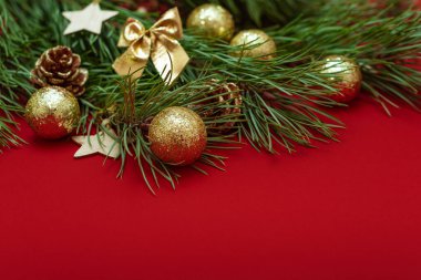 Parlak altın toplar, fiyonk, ahşap Noel oyuncakları ve çam kozalaklarıyla süslenmiş gür bir Noel ağacı dalı. Kırmızı arkaplanda Noel düzeni.