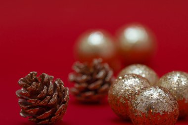 Minimalist Noel tebrik kartı şablonu, kırmızı arka planda çam kozalakları ve altın toplar.