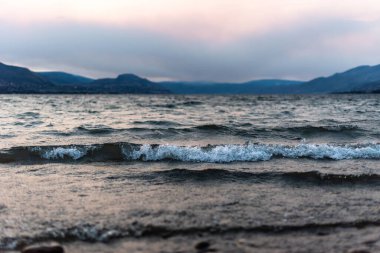 Yaz fırtınası sırasında Okanagan Gölü 'ndeki Three Mile Plajı' na yaklaşan bir dalganın yakın çekimi. Dağların üstünde alçak bulutlar...