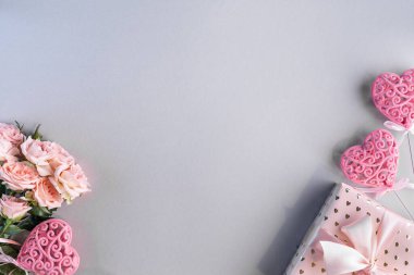 Pembe güllerle süslü bir çerçeve ve gri arka planda bir hediye. Üst manzara, düz yatış. Uzayı kopyala Doğum günü, anneler, sevgililer günü, kadınlar, düğün günü konsepti