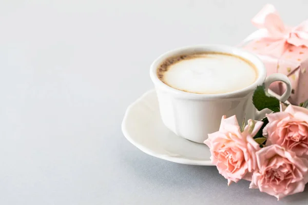 Cup of coffee, pink roses, box with a gift and pink roses on a gray background. Copy space.