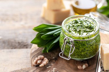 Tahta bir masada cam bir kavanozda zeytinyağı ve parmesan peynirli yaban pırasası pesto. Ramson 'ın kullanışlı özellikleri. Taze Ramson yaprakları.