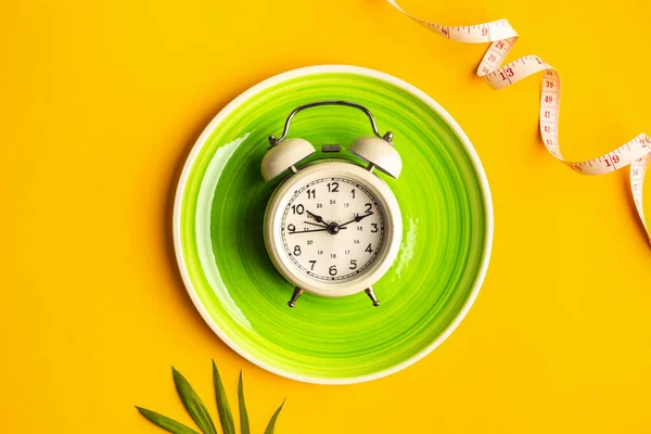 Composition with plate, alarm clock and measuring tape on a colored background. Diet concept and weight loss plan. — Stock fotografie