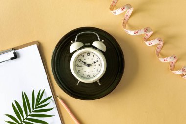 Composition with plate, alarm clock and measuring tape on a colored background. Diet concept and weight loss plan, copy space.