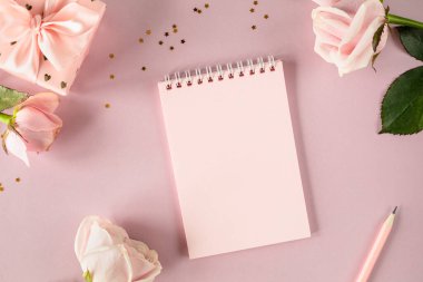 Açık pembe arka planda pembe güller ve hediye kutularıyla yazdığın metin için uzay not defterini kopyala. Düz yat. Üst görünüm.