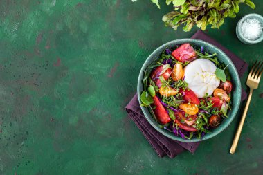Domatesli salata, roka, yeşil taşlı arka planda Burrata peyniri ve mikroyeşillikler.
