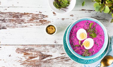 Pancar, salatalık ve ahşap zemin üzerinde mavi bir tabakta yumurtayla süslenmiş soğuk çorba. Üst görünüm.