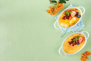 Yeşil bir masada taze çilek, üzümlü ve yaban mersinli iki creme brulee tatlısı..