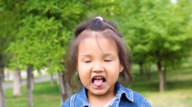 Parkta dilini gösteren sevimli küçük bir kızın portresi. 
