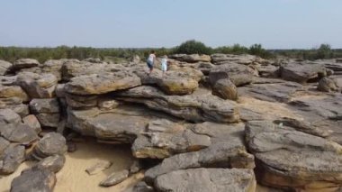 Hava görüntüsü. Anne ve çocuk yürürler ve büyük taş yığınına tırmanırlar. Kum taşların arasında görünür. Güneşli bir gün. Kız ve çocuk yaz tarzı giyinmiş, şort ve elbise giymişler..