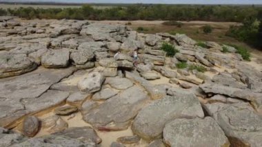 Hava görüntüsü. Anne ve çocuk yürürler ve büyük taş yığınına tırmanırlar. Kum taşların arasında görünür. Güneşli bir gün. Kız ve çocuk yaz tarzı giyinmiş, şort ve elbise giymişler..
