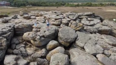 Hava görüntüsü. Anne ve çocuk yürürler ve büyük taş yığınına tırmanırlar. Kum taşların arasında görünür. Güneşli bir gün. Kız ve çocuk yaz tarzı giyinmiş, şort ve elbise giymişler..