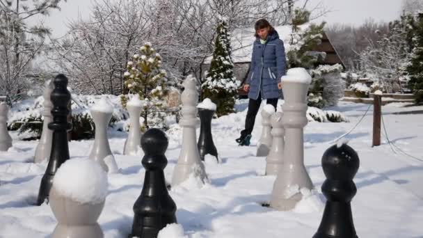 少女は雪の中でチェスの駒を調べる 屋外プレイのための素晴らしいアイテム 屋外ゲーム — ストック動画