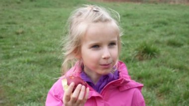 Dışarıda taze çimenlerin üzerinde elma yiyen bir kız..