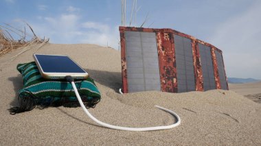 Güneş paneli, kumlu çölde akıllı telefonu dağların arka planına karşı şarj ediyor.