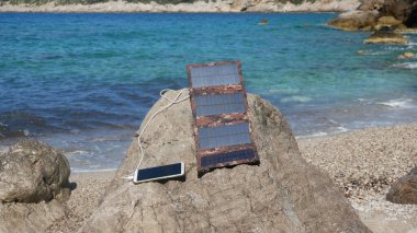 Güneş paneli deniz kıyısındaki akıllı telefonu şarj ediyor.