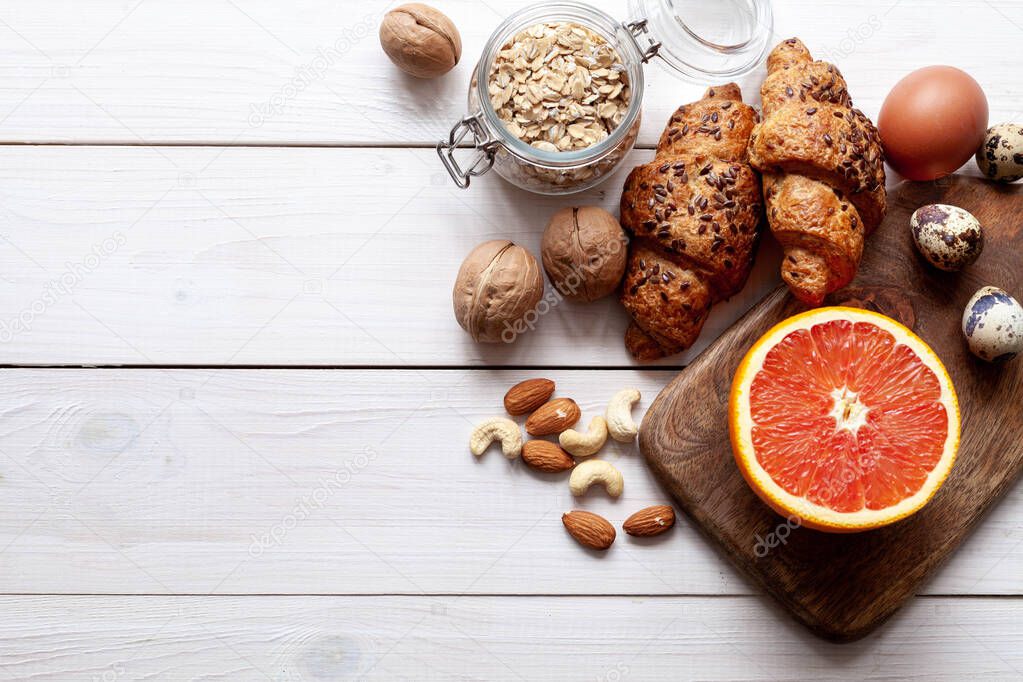 White wood background with organic food: grapefruit, cereal, nuts and eggs, top view