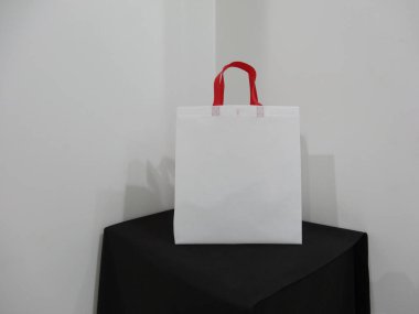 Beautiful Non Woven grocery shopping white bag with red handle loop isolated on black table against white wall background