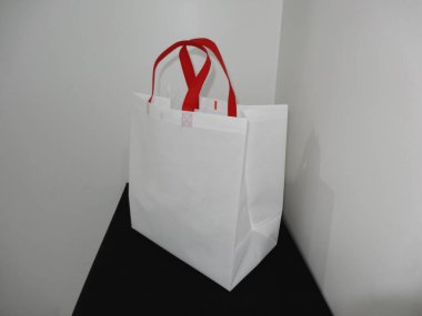 Beautiful Non Woven grocery shopping white bag with red handle loop isolated on black table against white wall background