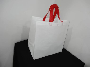 Beautiful Non Woven grocery shopping white bag with red handle loop isolated on black table against white wall background