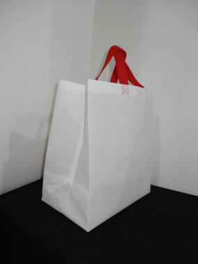 Beautiful Non Woven grocery shopping white bag with red handle loop isolated on black table against white wall background