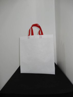 Beautiful Non Woven grocery shopping white bag with red handle loop isolated on black table against white wall background