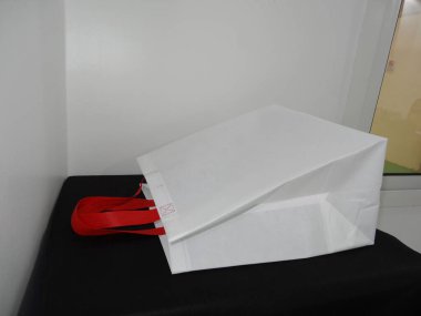 Beautiful Non Woven grocery shopping white bag with red handle loop isolated on black table against white wall background