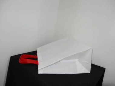 Beautiful Non Woven grocery shopping white bag with red handle loop isolated on black table against white wall background