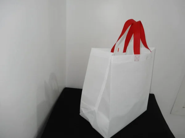 Beautiful Non Woven grocery shopping white bag with red handle loop isolated on black table against white wall background