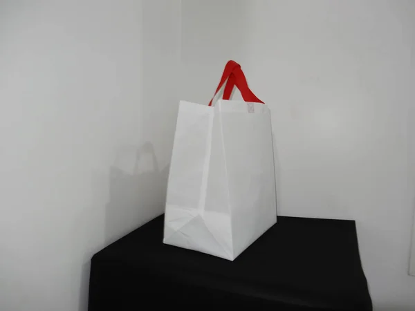 Beautiful Non Woven grocery shopping white bag with red handle loop isolated on black table against white wall background