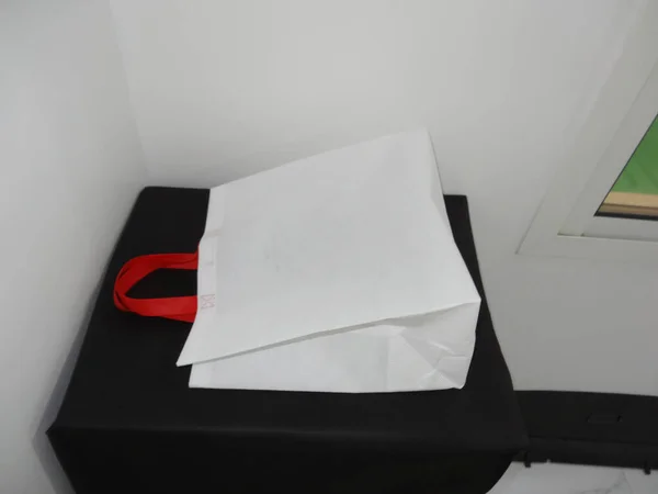 Beautiful Non Woven grocery shopping white bag with red handle loop isolated on black table against white wall background